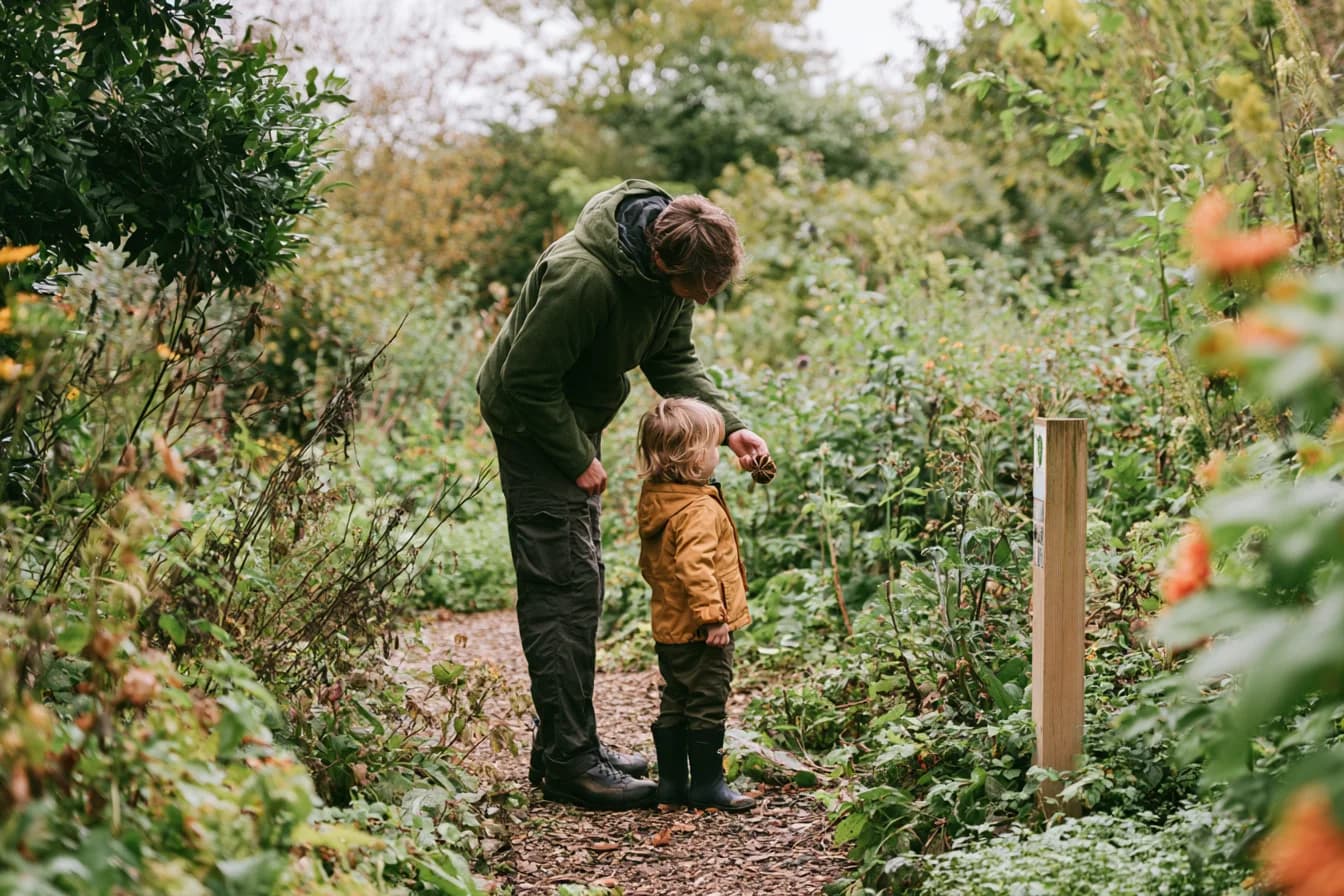 An adult and child discovering a seed pod beside a garden trail marker.